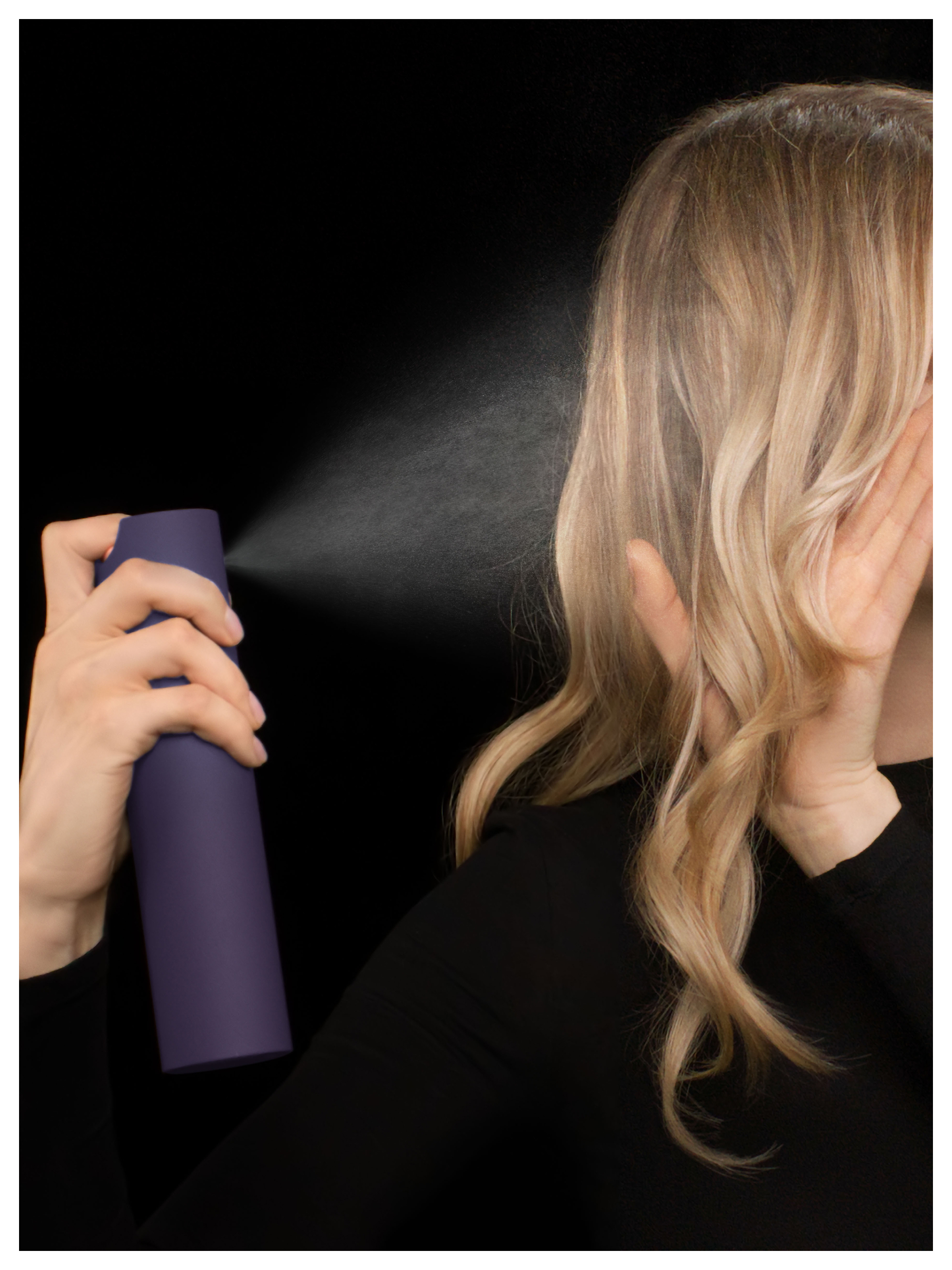 Eine Hand hält eine lila Sprühdose, die Haarspray auf blondes Haar sprüht.