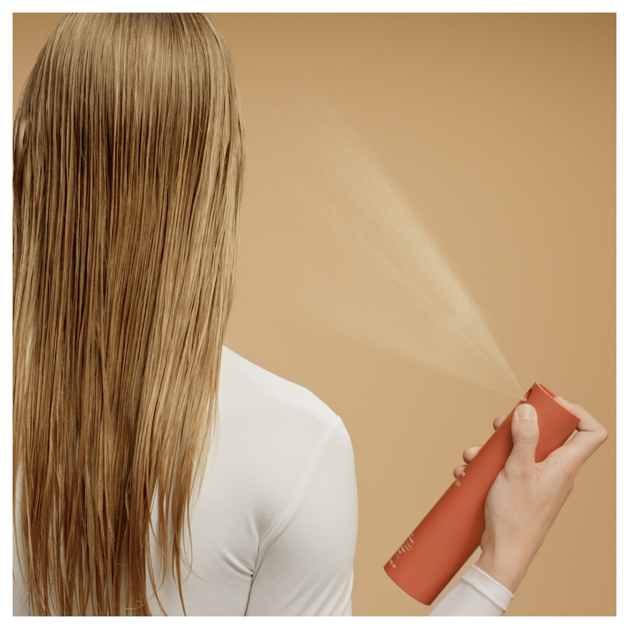 Eine Hand sprüht ein Produkt auf das nasse blonde Haar einer Person.