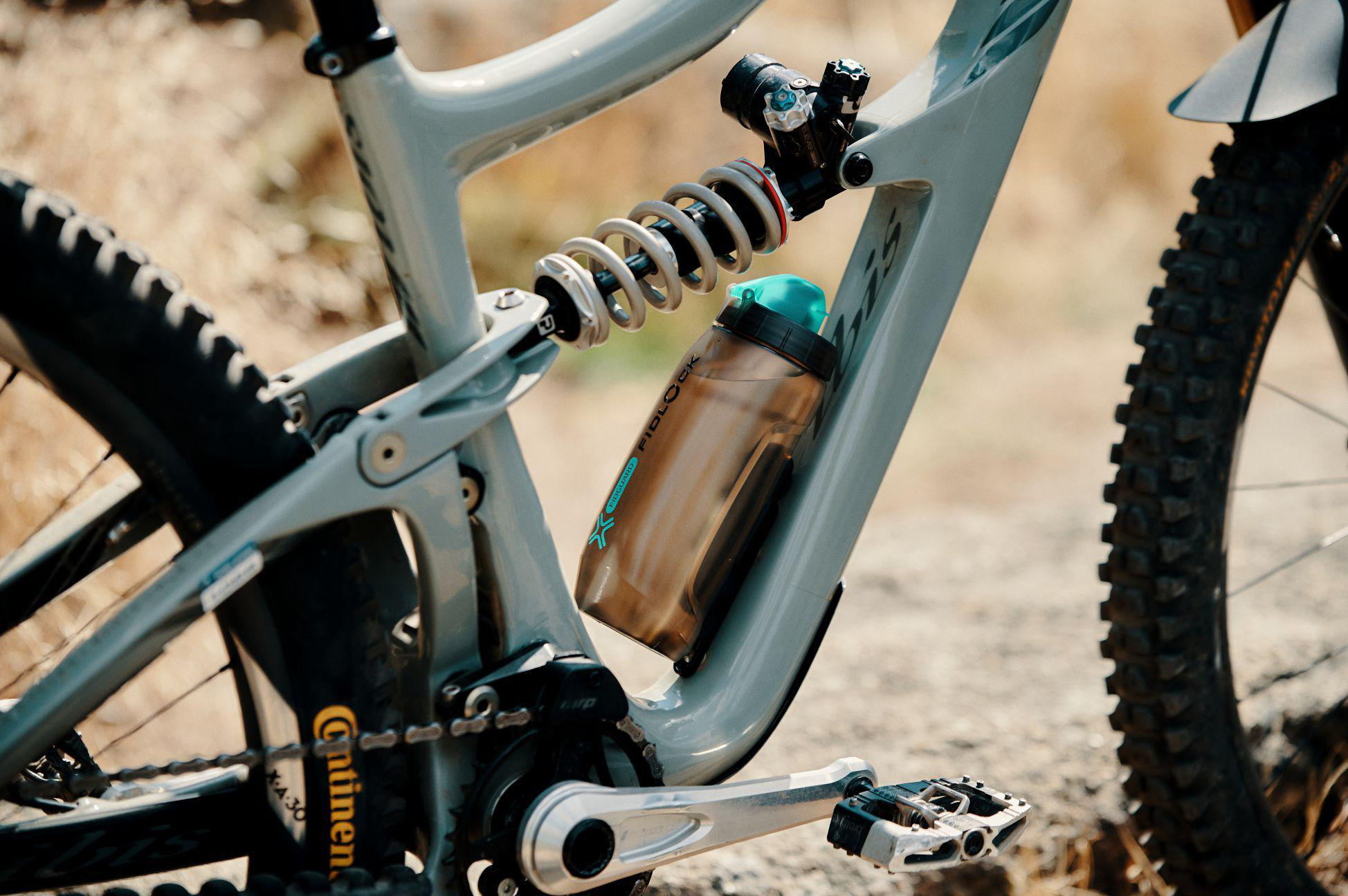 Nahaufnahme eines grauen Full-Suspension Mountainbikes mit Wasserflasche und Stoßdämpfer.