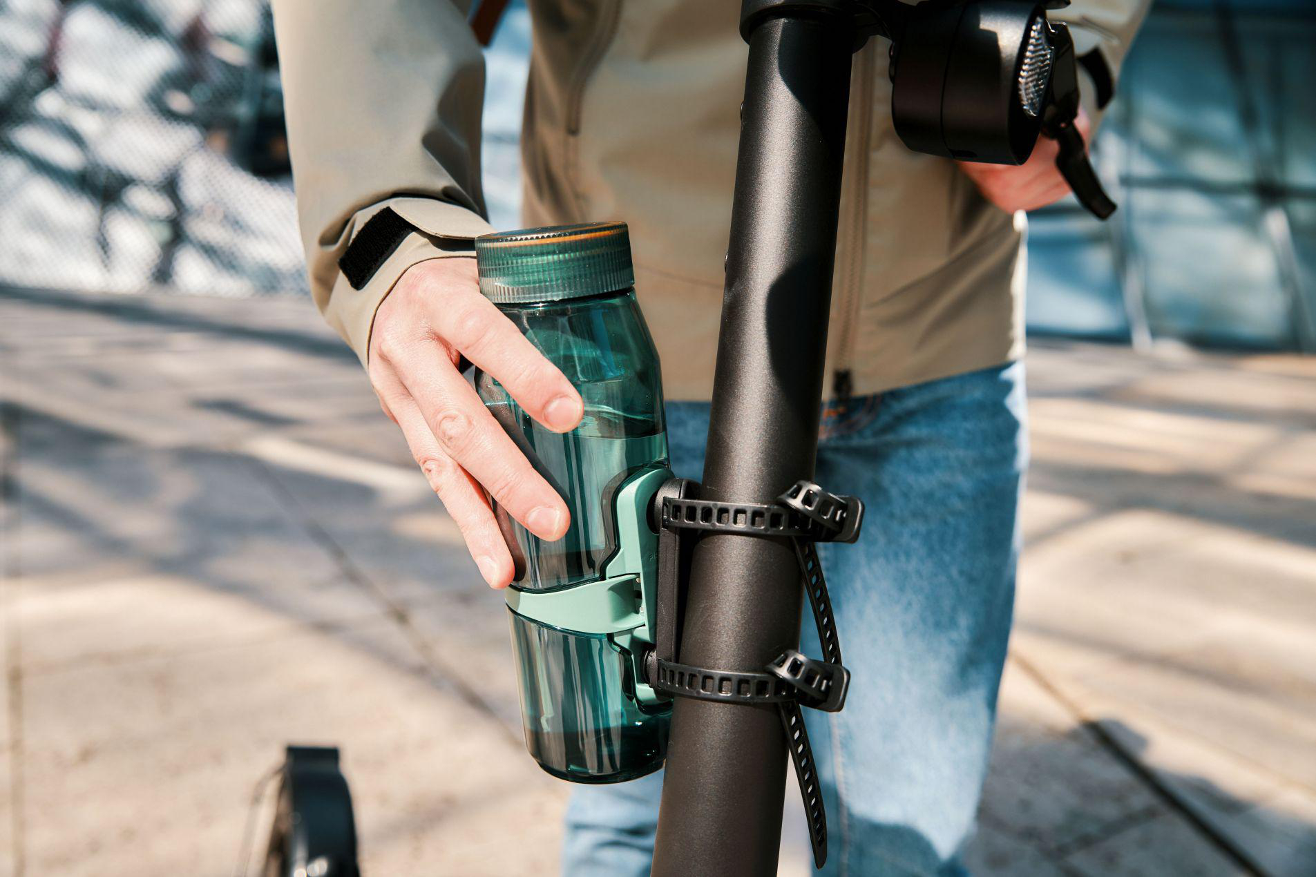 Eine Hand hält eine grüne Wasserflasche an einer E-Scooter-Stange.