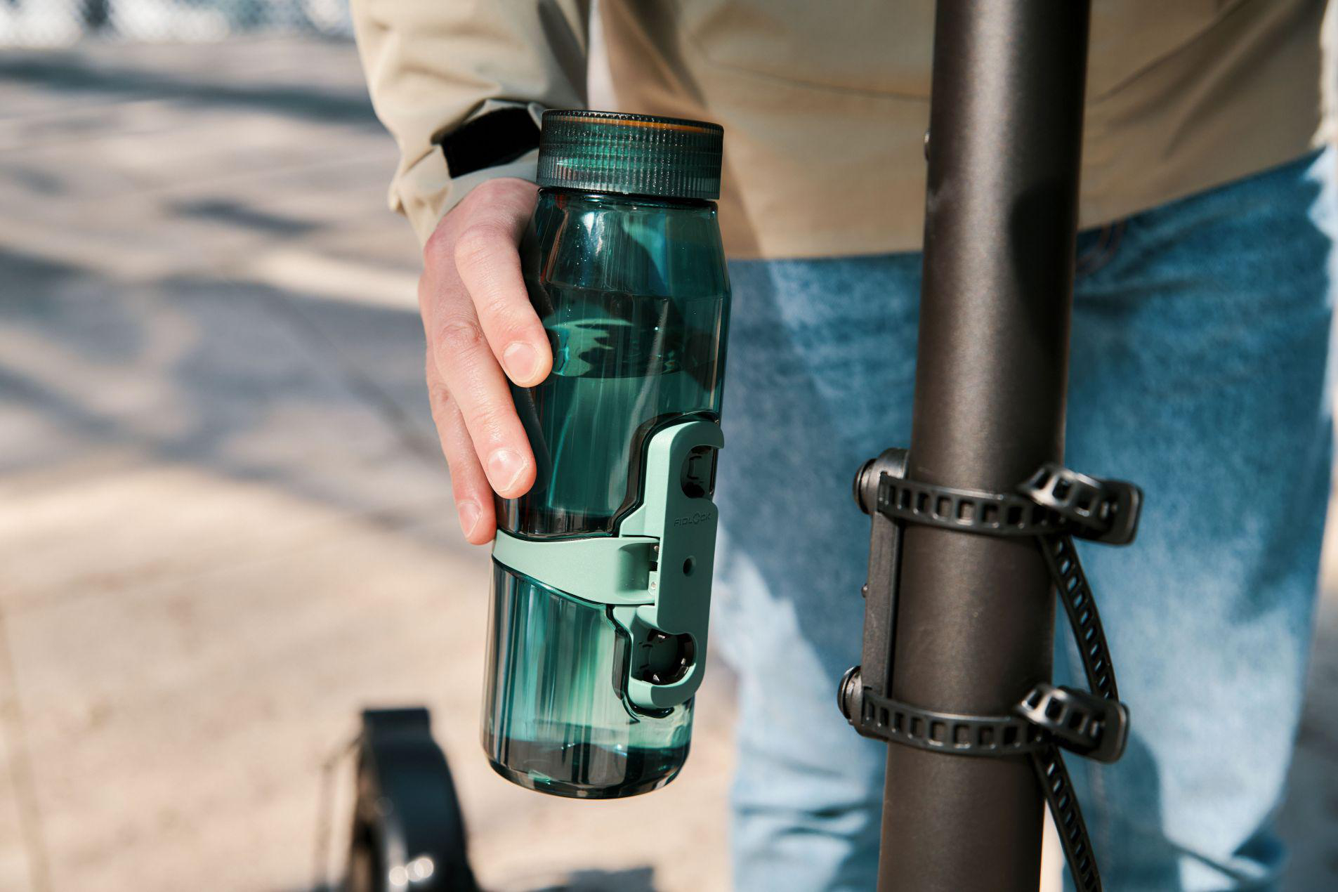 Eine Hand hält eine dunkelgrüne Wasserflasche an einem Roller.