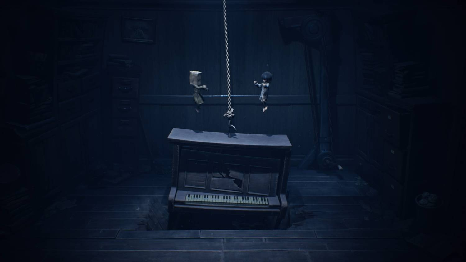 Dos niños cuelgan de una cuerda sobre un piano en una habitación oscura.