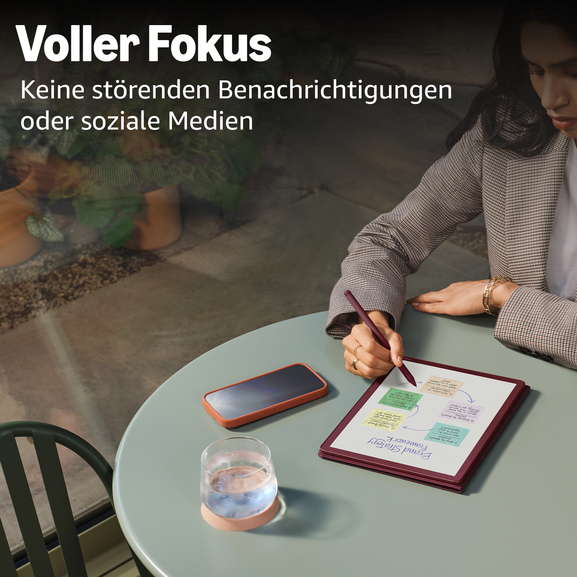 Eine Frau schreibt auf einem Tablet, daneben liegen ein Handy und ein Glas Wasser.