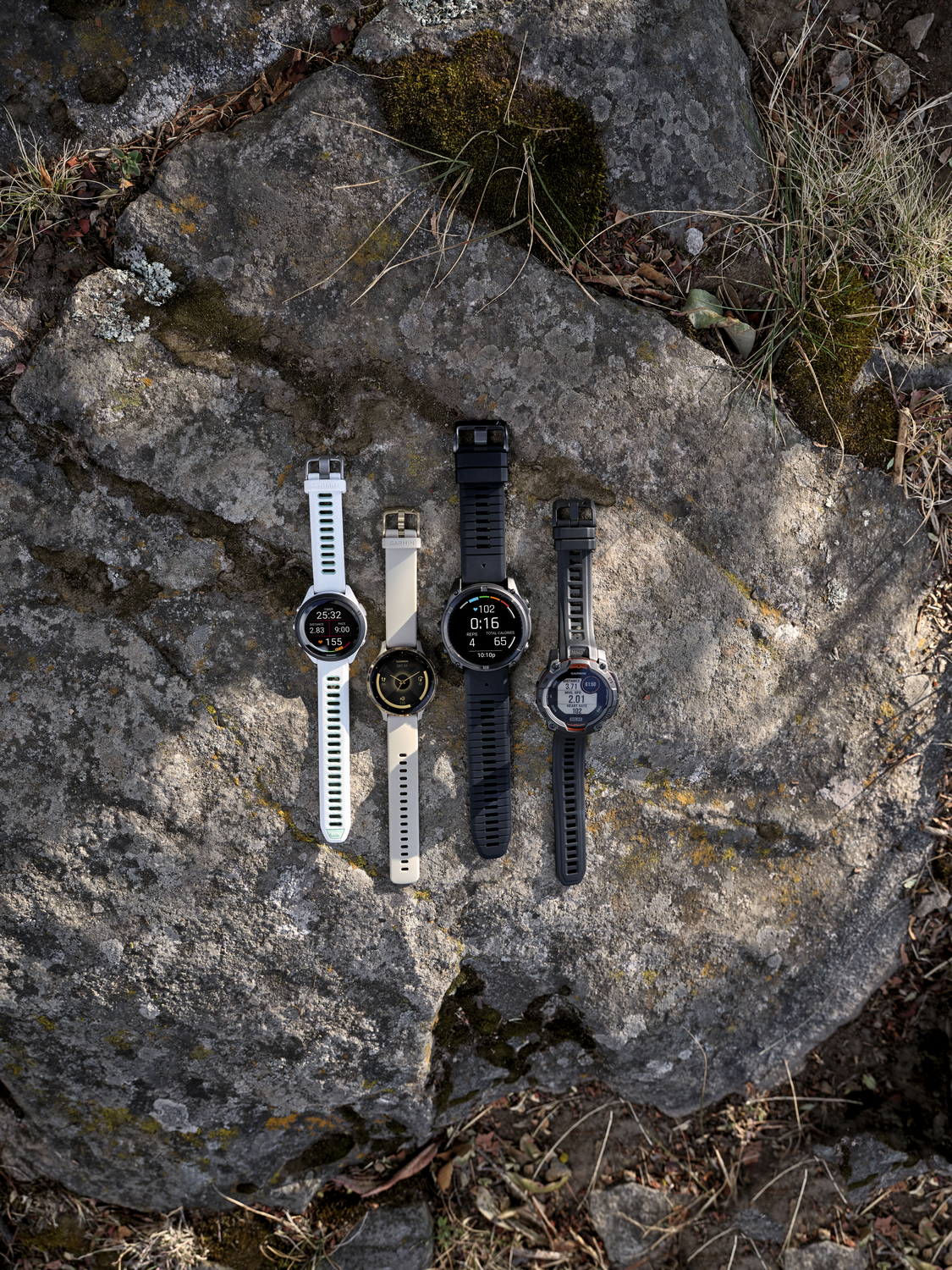 Cuatro relojes inteligentes sobre una roca. De izquierda a derecha: blanco, beige, negro, gris oscuro.