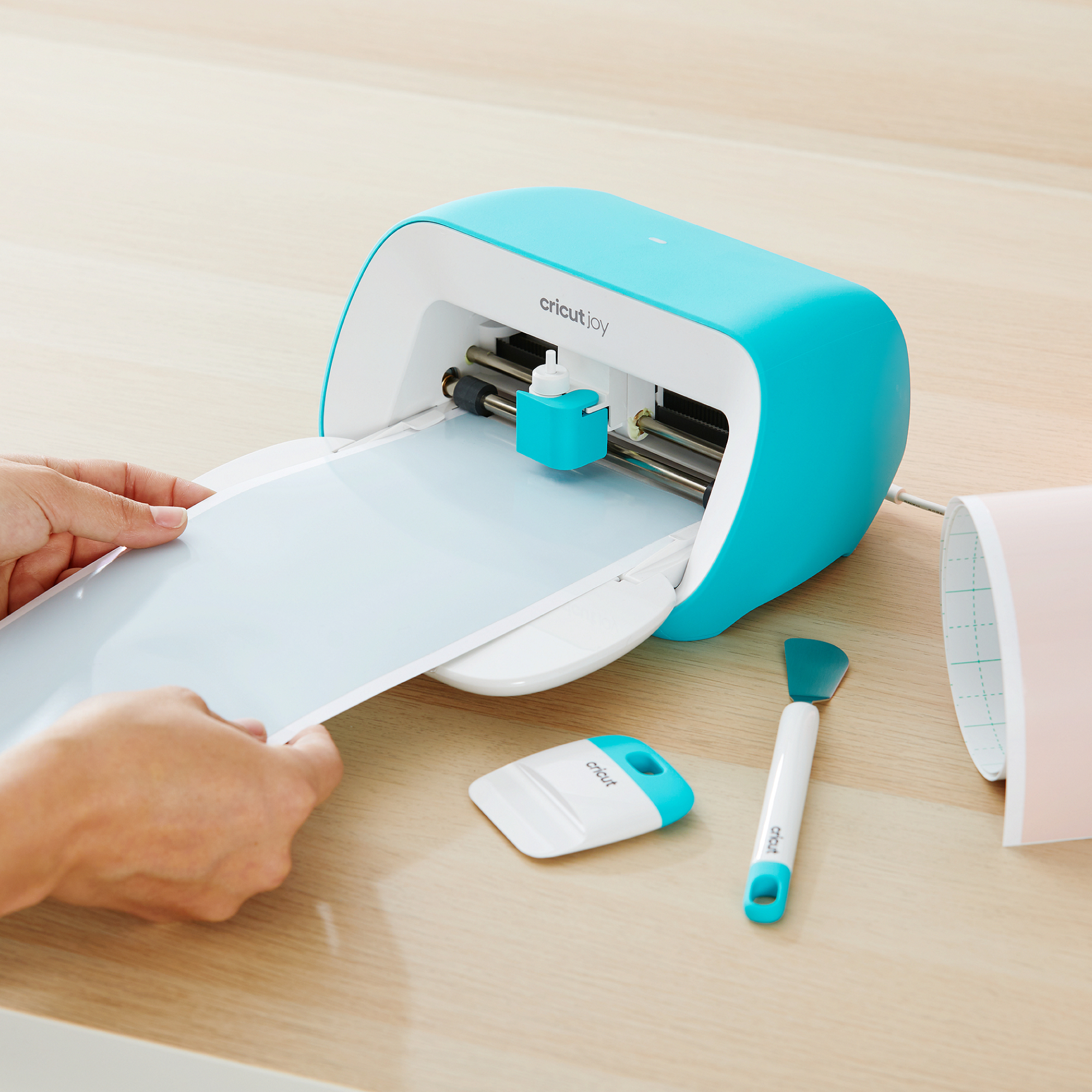 Una persona coloca una lámina azul claro en una máquina de corte Cricut Joy turquesa.