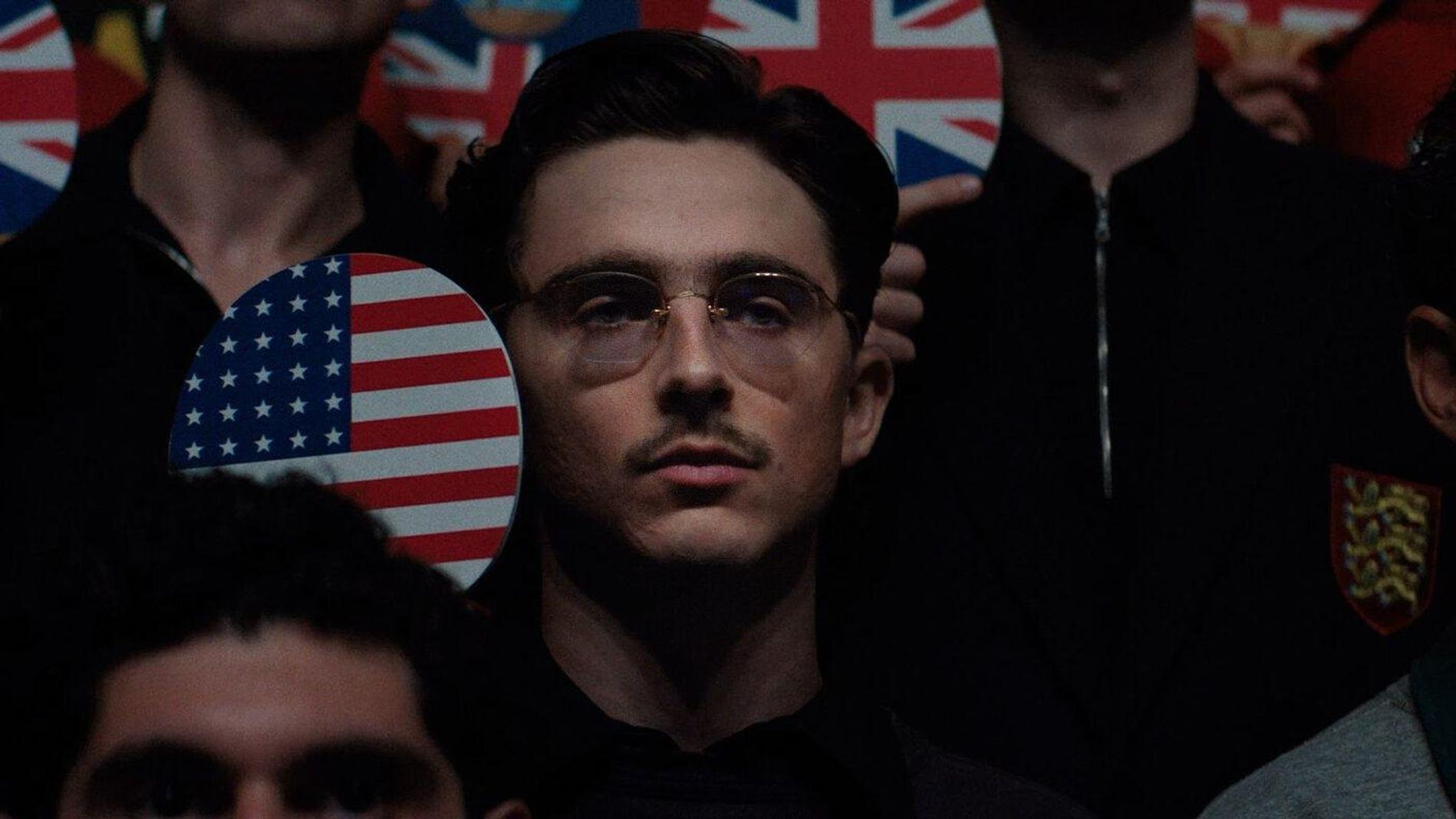 Mann mit Brille vor Flaggen, hält amerikanische Flagge.