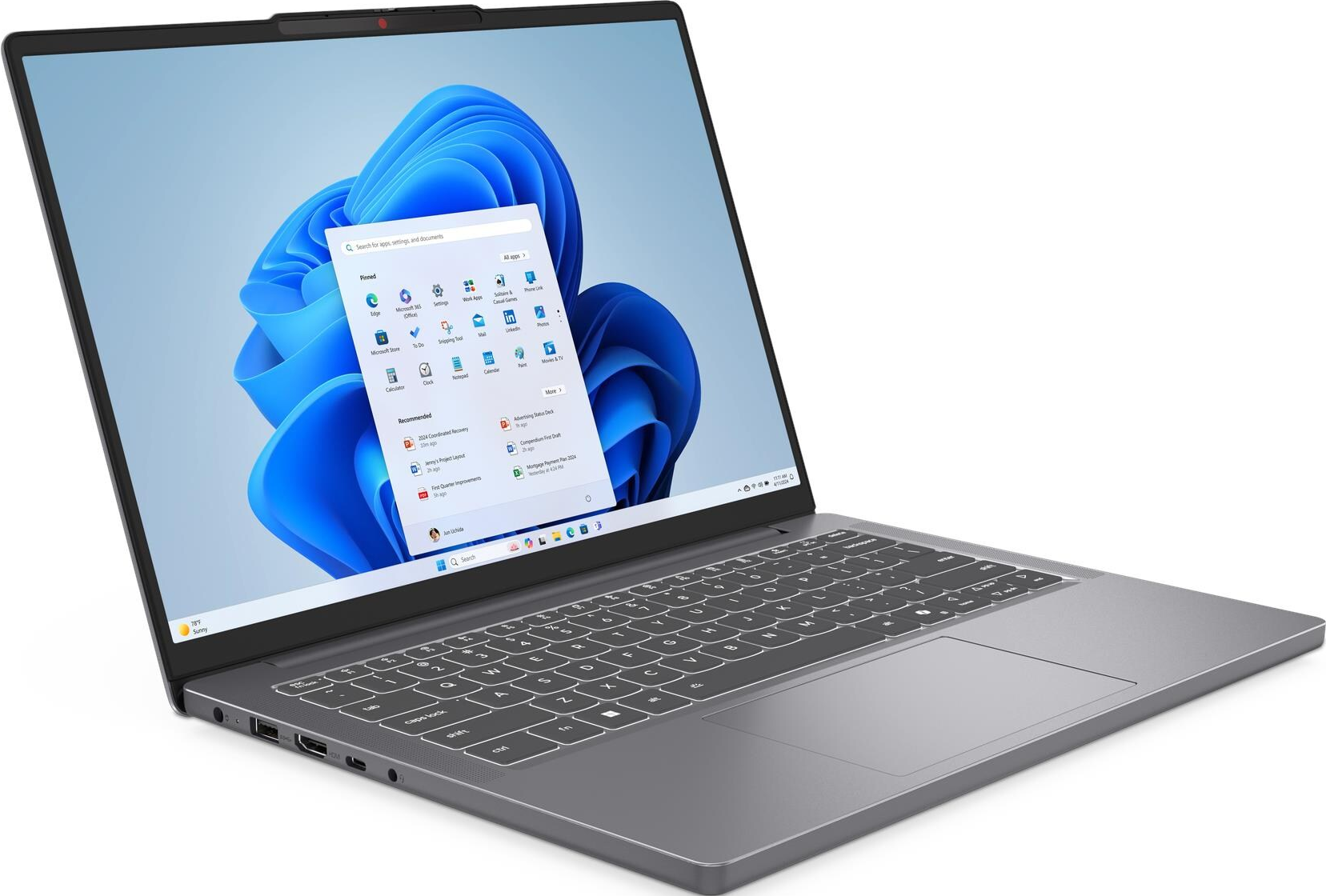 Un laptop grigio mostra Windows 11 con sfondo astratto blu e menu.