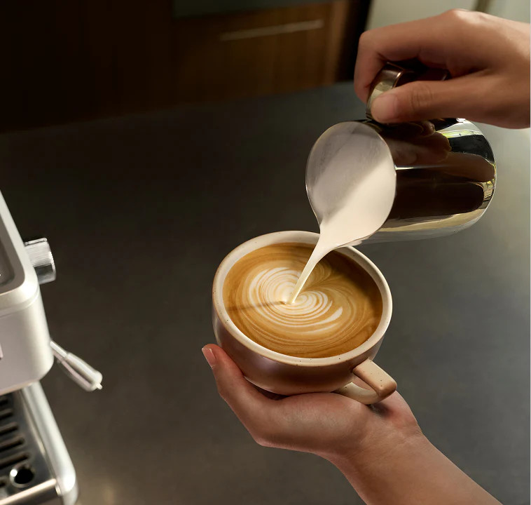 Osoba nalewa spienione mleko do filiżanki kawy, tworząc latte art.
