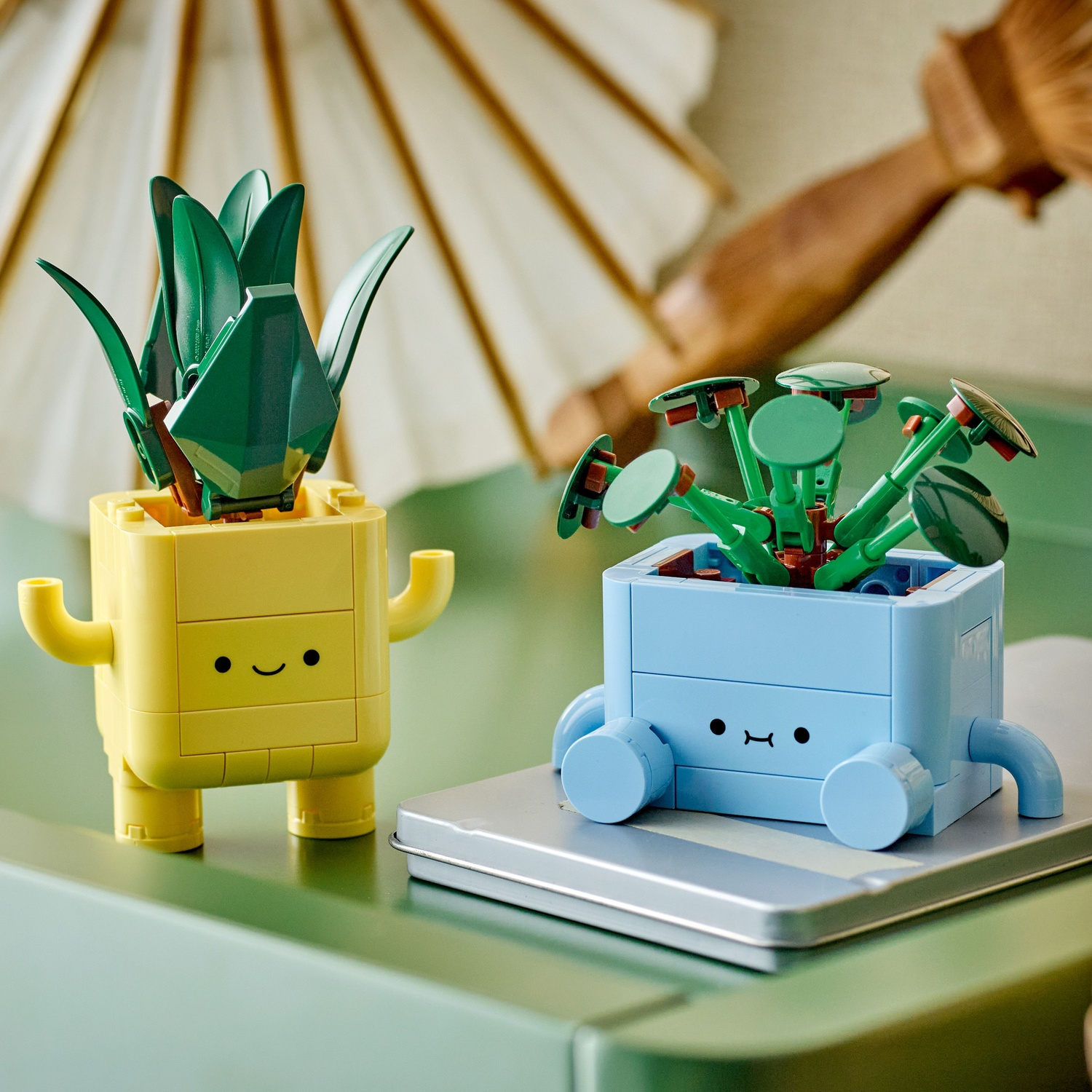 Twee Lego potplanten, een gele met armen en benen, een blauwe op wielen.