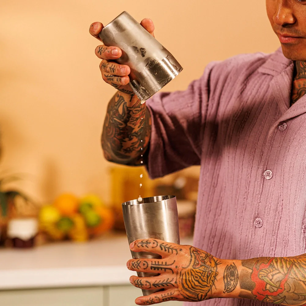 Ein Mann mit Tattoos schüttet Flüssigkeit aus einem Metallbecher in einen anderen.