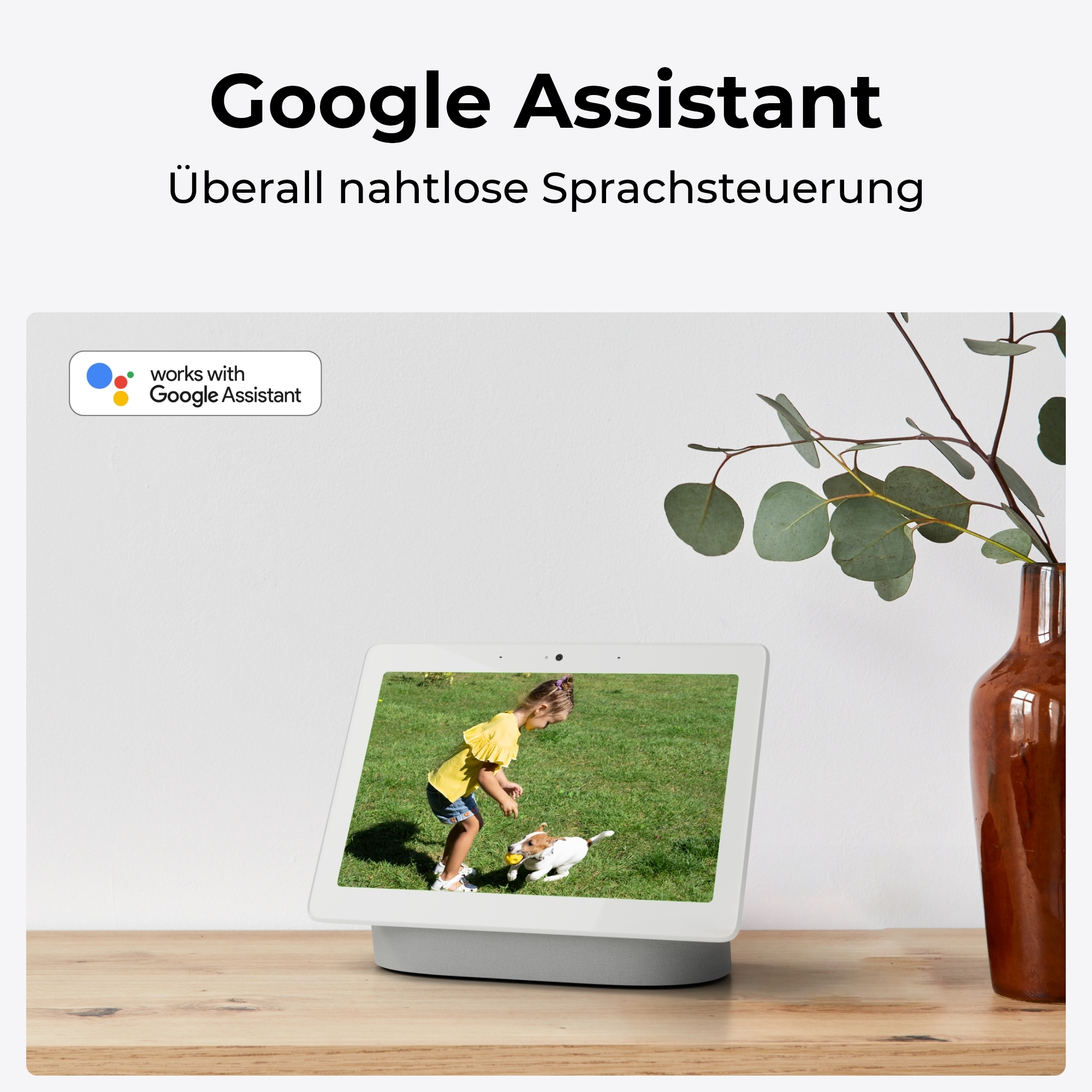 Ein Mädchen spielt mit einem Hund im Gras vor einem Google Assistant Display.