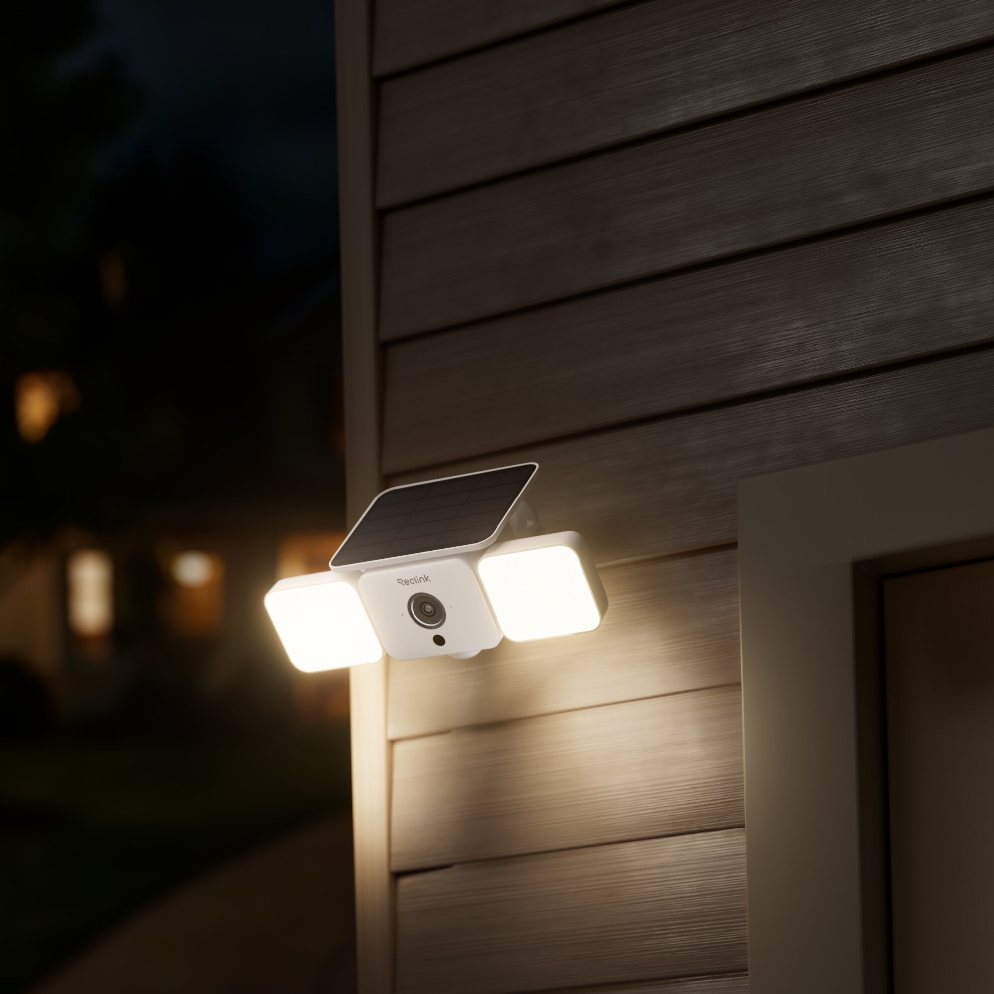 Eine weiße Überwachungskamera mit Solarpanel und zwei Lichtern montiert an einer Hauswand.