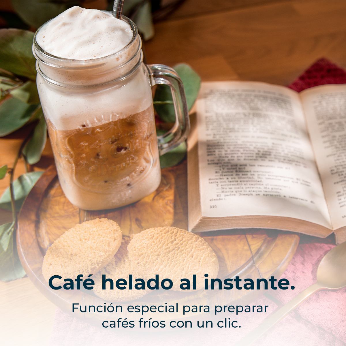 Café helado en vaso con espuma, galletas y un libro al lado.