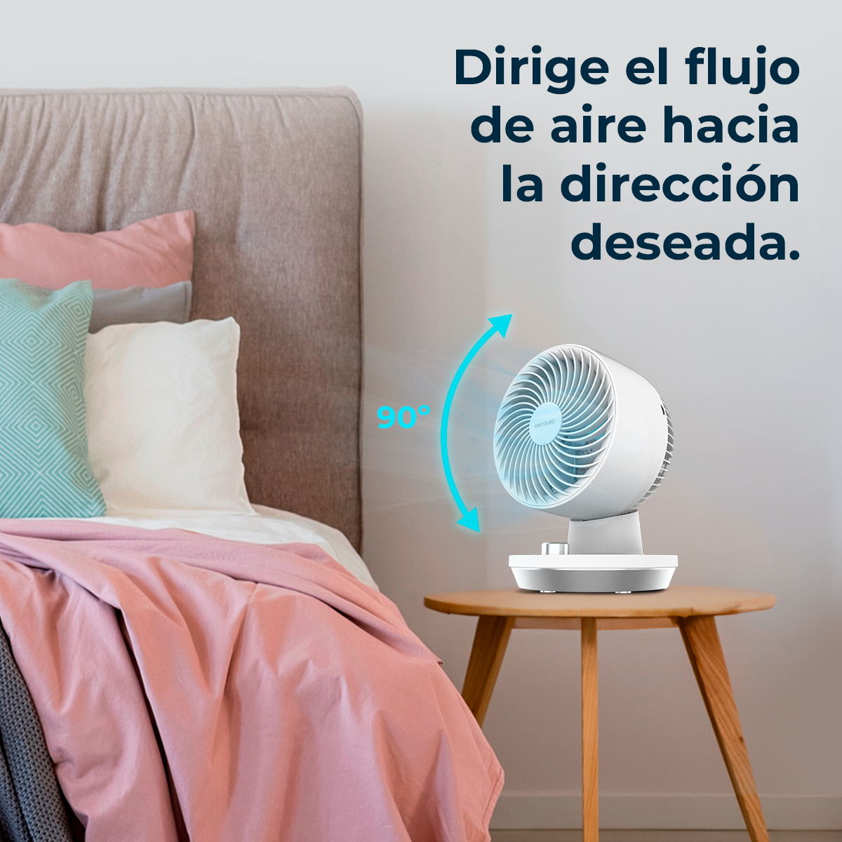 Un ventilador blanco sobre una mesa de madera junto a una cama con mantas rosas.