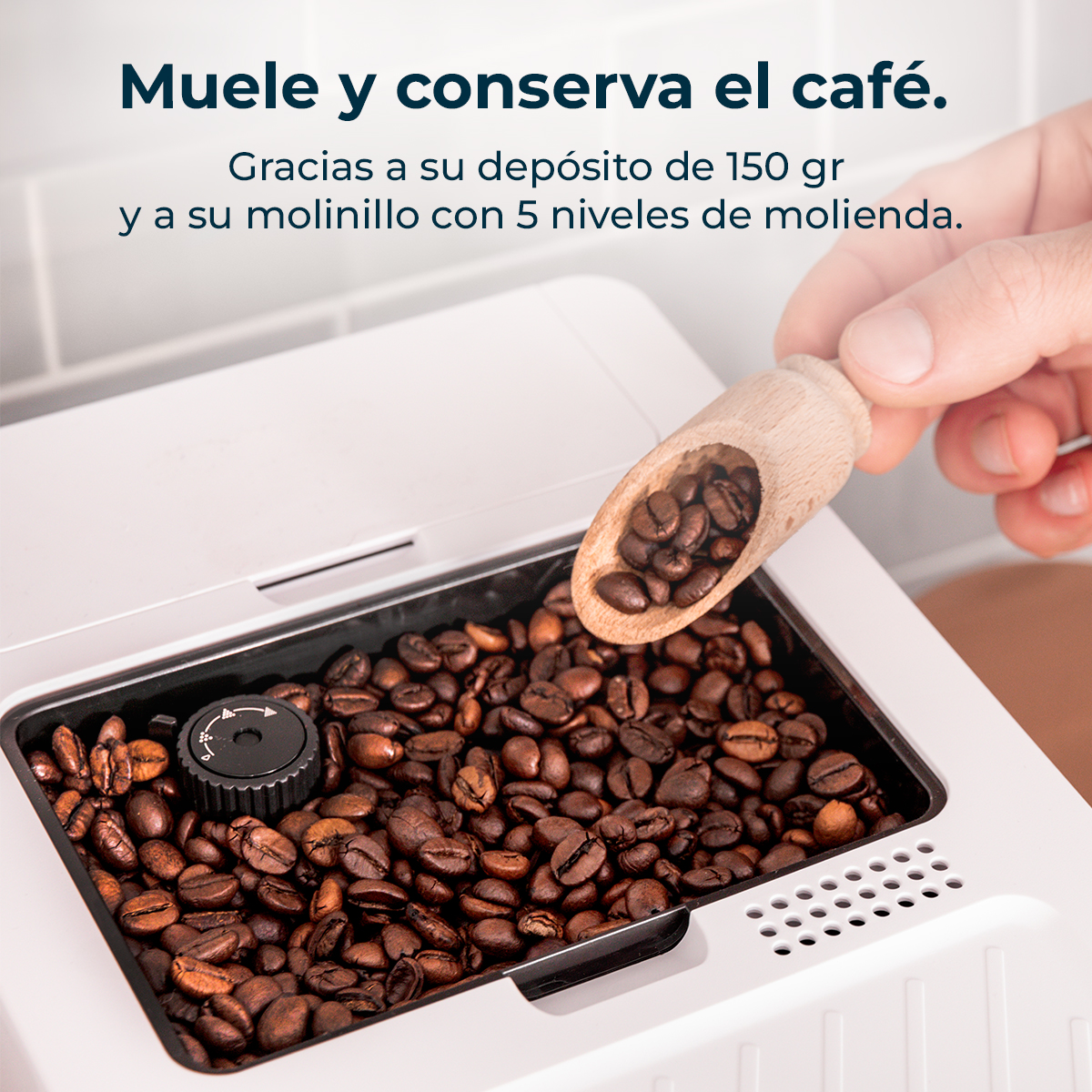 Una mano vierte granos de café en la tolva de un molinillo blanco con una cuchara de madera.