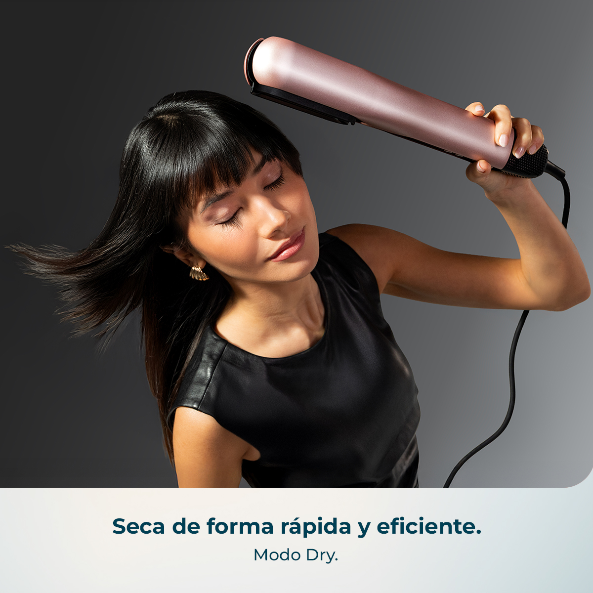 Una mujer de pelo oscuro usa un secador de pelo rosa dorado.