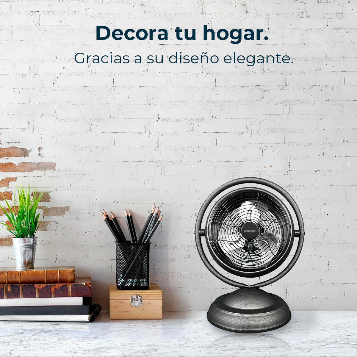 Un ventilador plateado se sienta en un escritorio junto a libros y lápices.