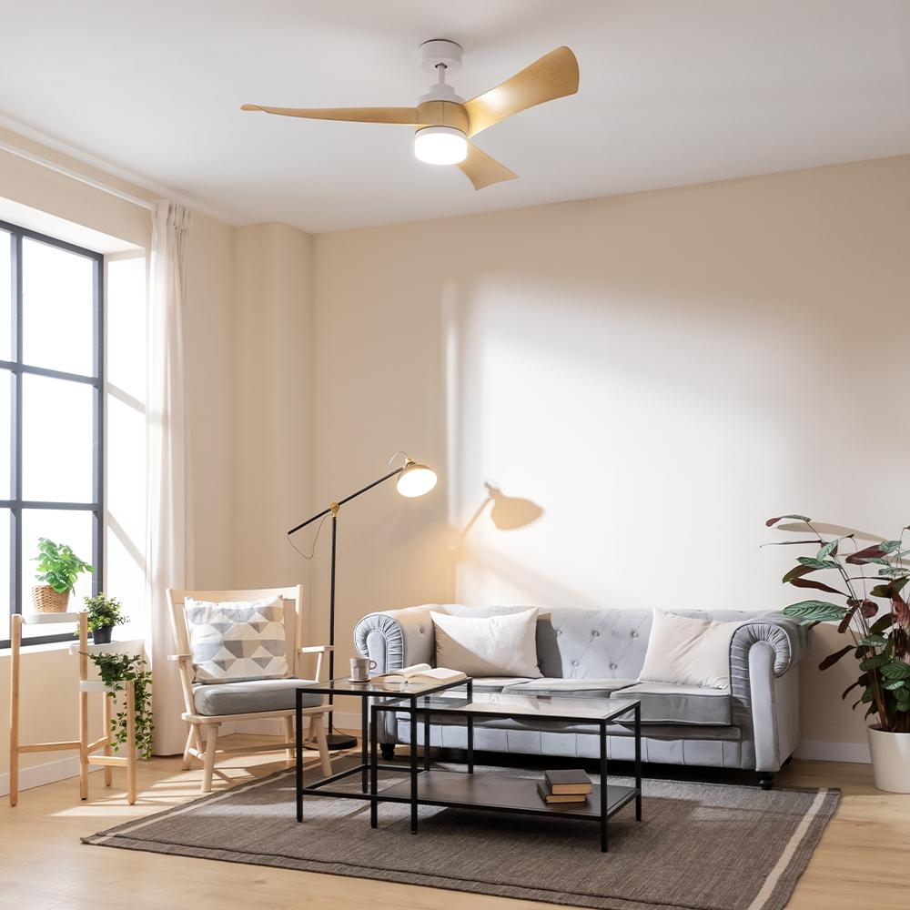 Una sala de estar luminosa con sofá, sillón, mesas de centro, lámpara y ventilador de techo.
