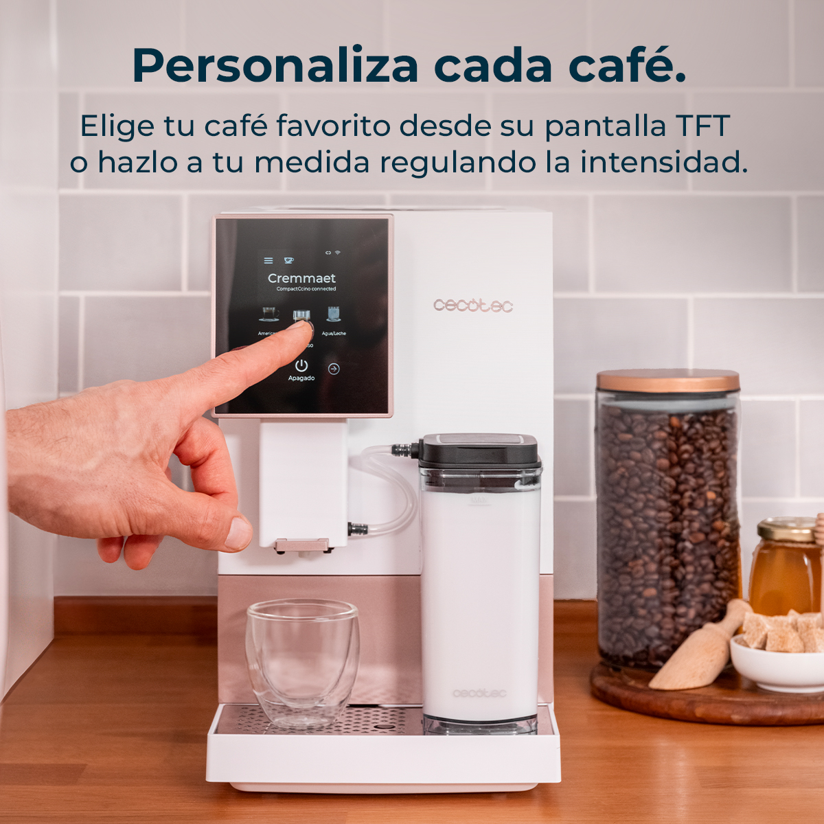 Una mano opera una cafetera blanca con pantalla TFT. Hay granos de café y miel cerca.