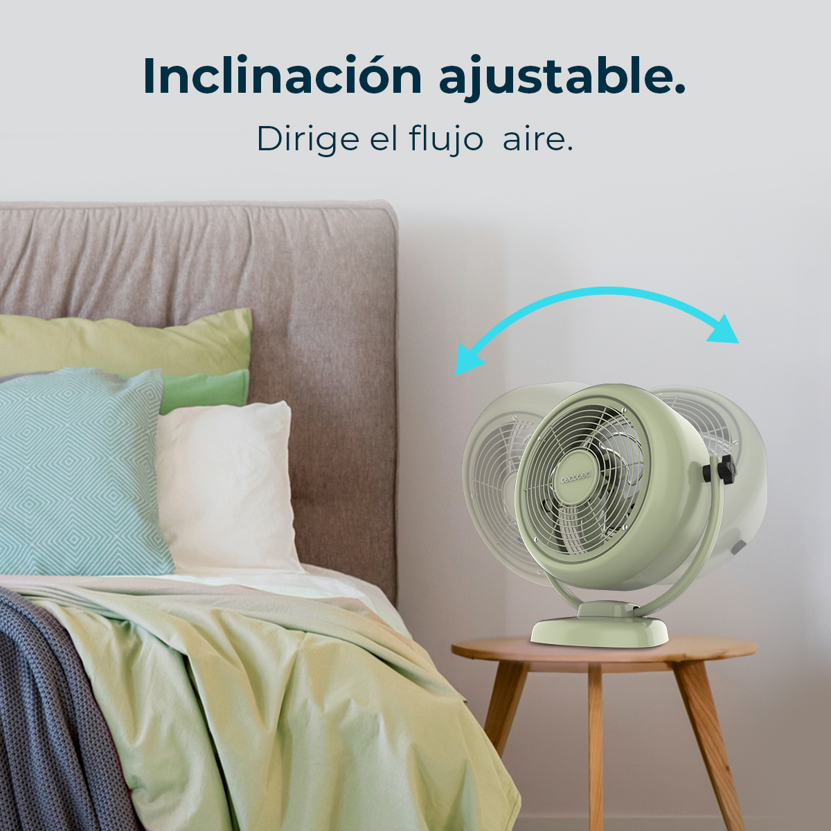 Un ventilador verde sobre una mesa de madera junto a una cama con cojines verdes y azules.