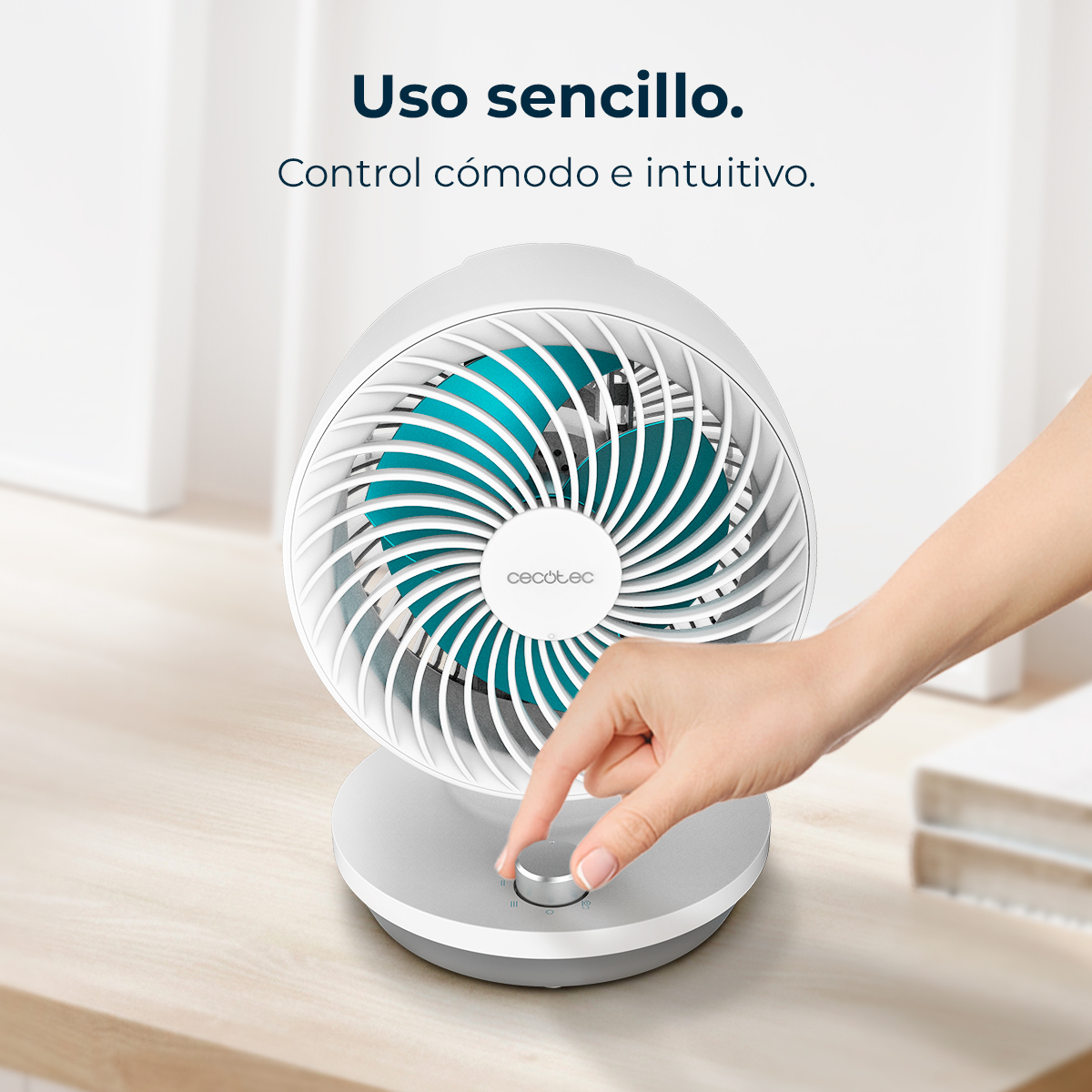 Una mano gira el mando de un ventilador blanco con aspas turquesas.