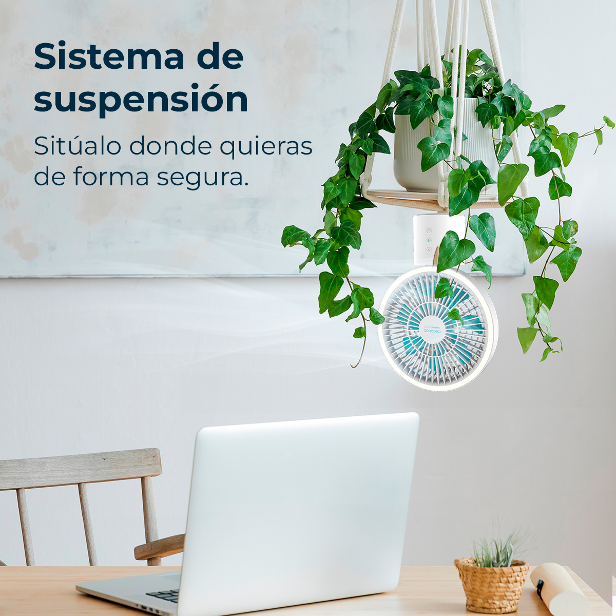 Un ventilador blanco con aspas azules cuelga de una cuerda junto a una planta. Un portátil está sobre una mesa.