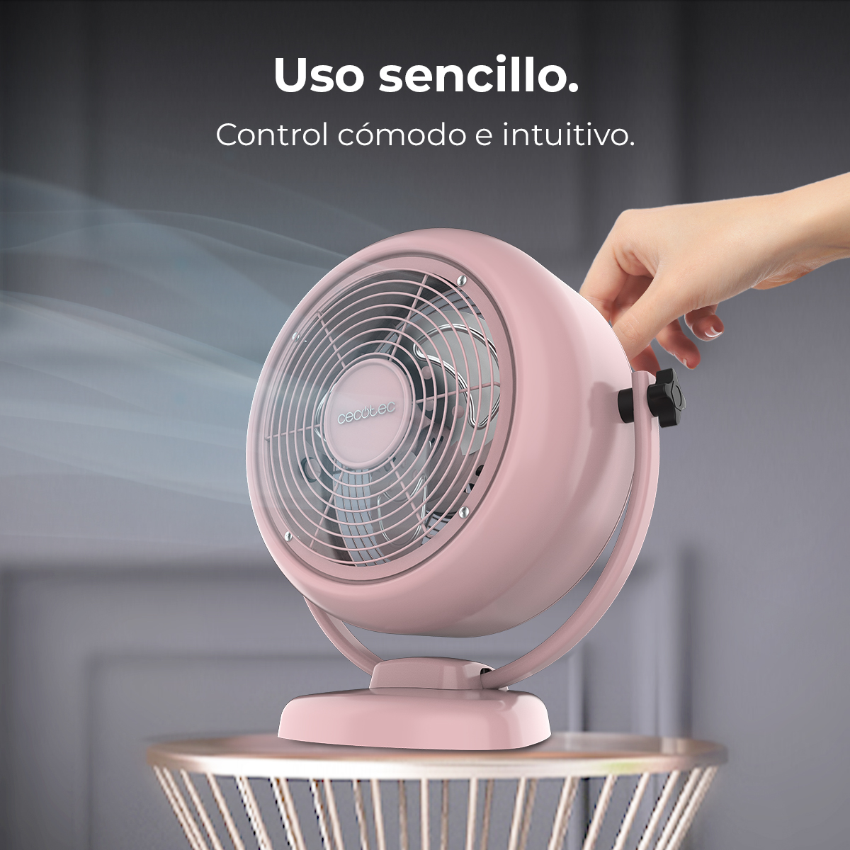 Un ventilador de mesa rosa con logo Cecotec sobre una mesa de alambre.