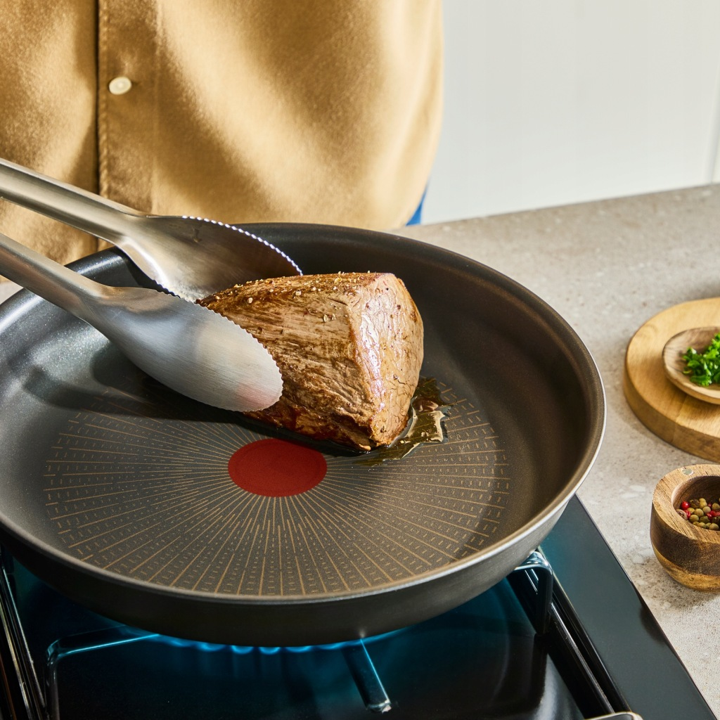 Kawałek pieczeni jest obracany w patelni na kuchence za pomocą szczypiec.