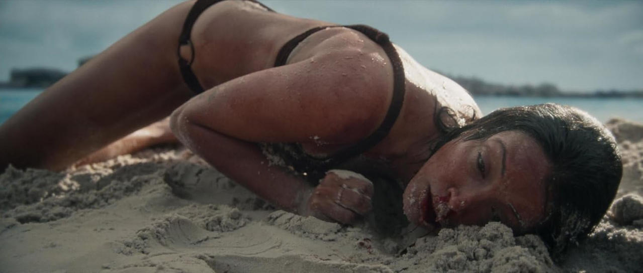 Eine Frau in einem Bikini liegt auf dem Sand am Strand, mit dem Gesicht nach unten.