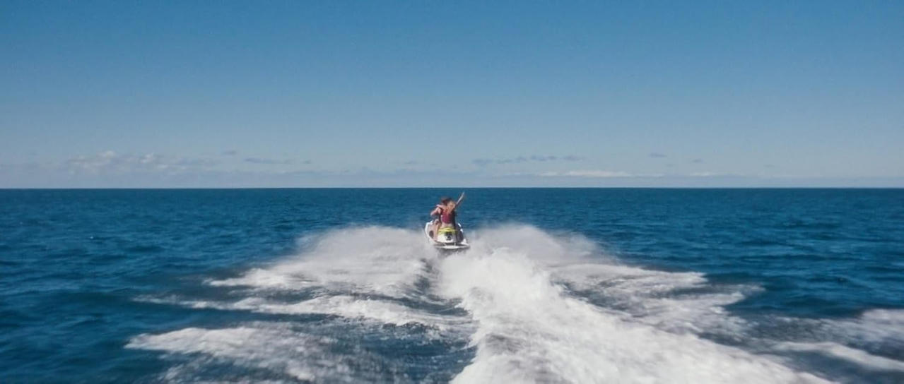 Zwei Personen auf einem Jetski fahren auf dem blauen Meer, der Himmel ist klar.