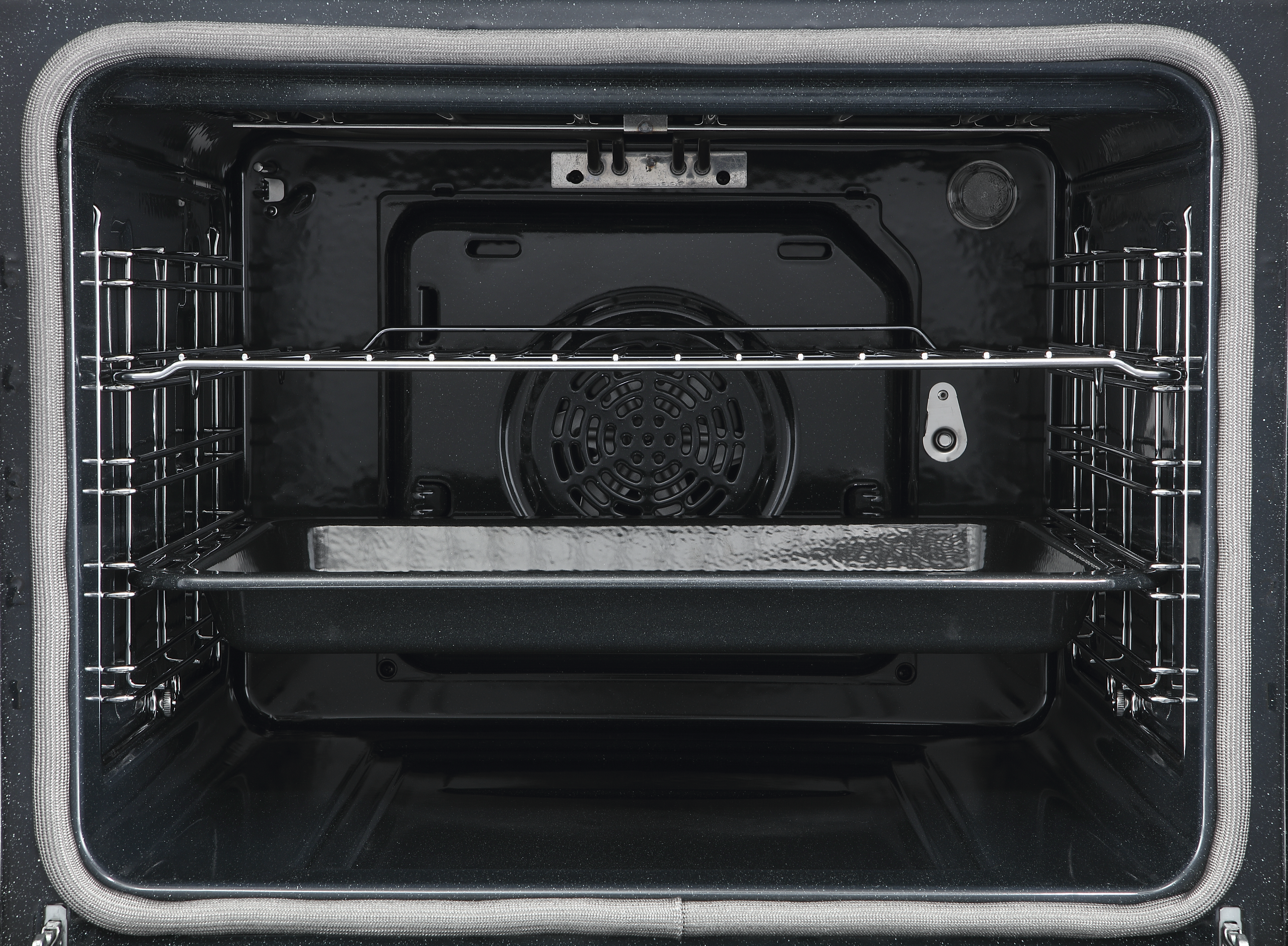 Puste wnętrze piekarnika z rusztami, blachą i kratką wentylatora.
