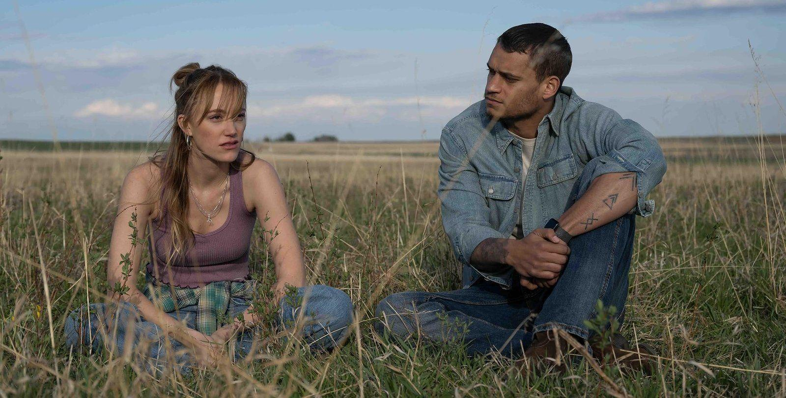 Ein Mann und eine Frau sitzen in einem Feld unter blauem Himmel.