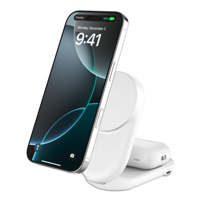 Un cargador inalámbrico Belkin blanco sostiene un iPhone plateado y un estuche de auriculares.