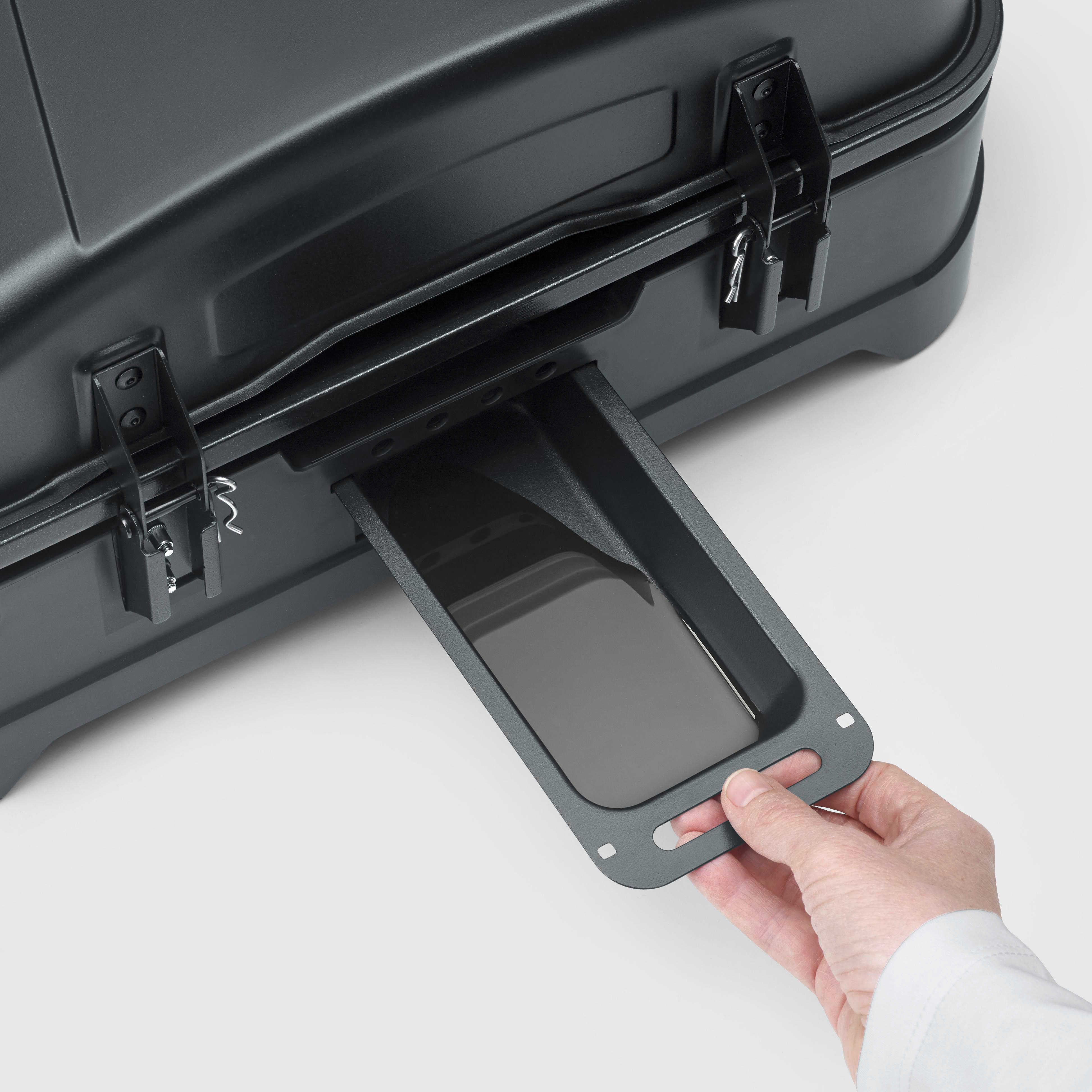 Eine Hand zieht eine Schublade mit einem Smartphone aus einem schwarzen Koffer.
