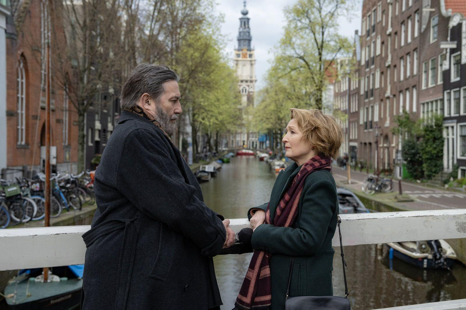 Ein Mann und eine Frau stehen auf einer Brücke in Amsterdam und blicken sich an.