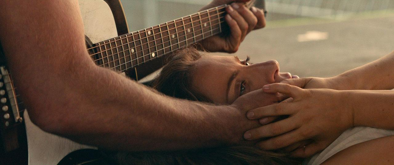Nahaufnahme einer Frau, die auf dem Schoß eines Mannes liegt, der eine Gitarre spielt.