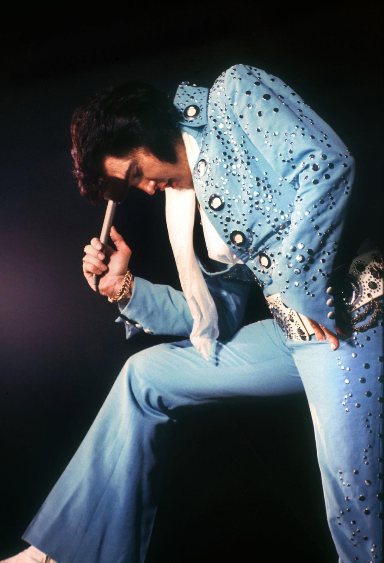 Elvis Presley im blauen Jumpsuit mit Strasssteinen, Mikrofon haltend.