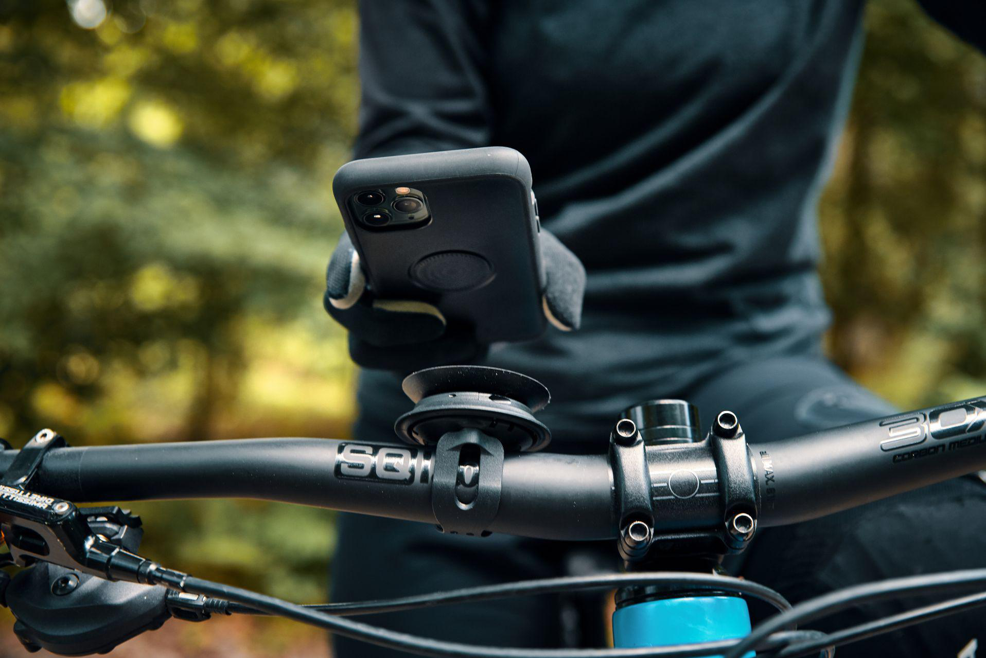 Person hält Handy über Fahrradlenker mit Wald im Hintergrund.