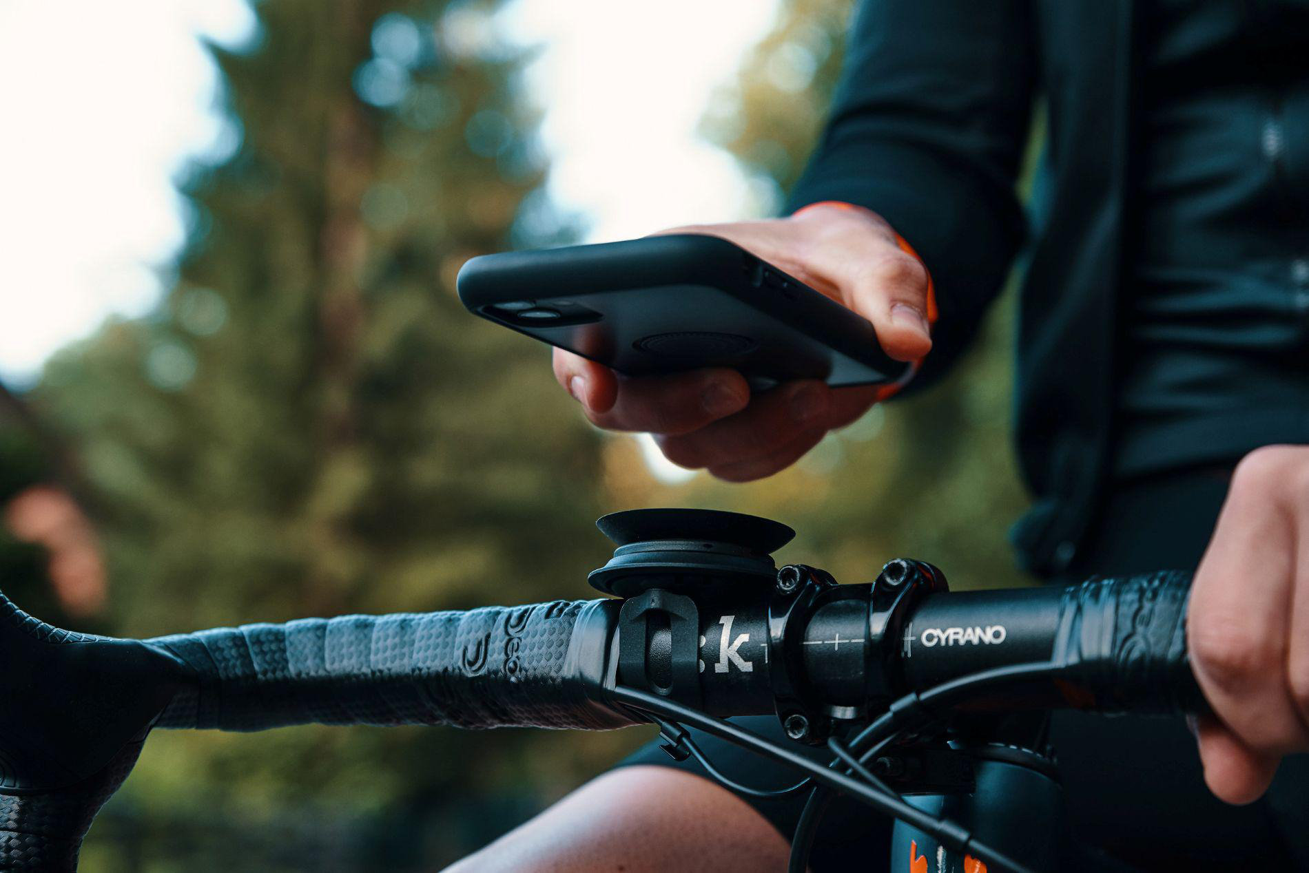 Eine Hand hält ein schwarzes Smartphone über einen Fahrradlenker mit Halterung.
