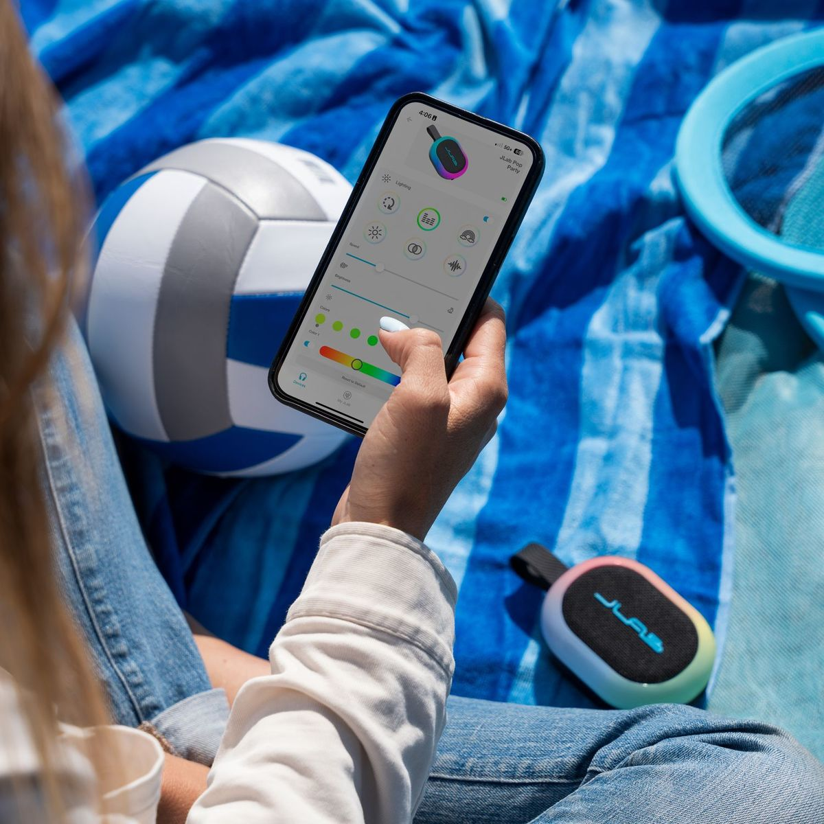 Eine Person hält ein Smartphone mit einer App, neben einem Volleyball und einem Lautsprecher.
