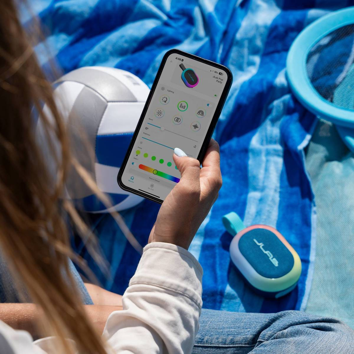 Eine Person bedient ein Smartphone mit einer App, daneben ein kleiner Lautsprecher und ein Volleyball.