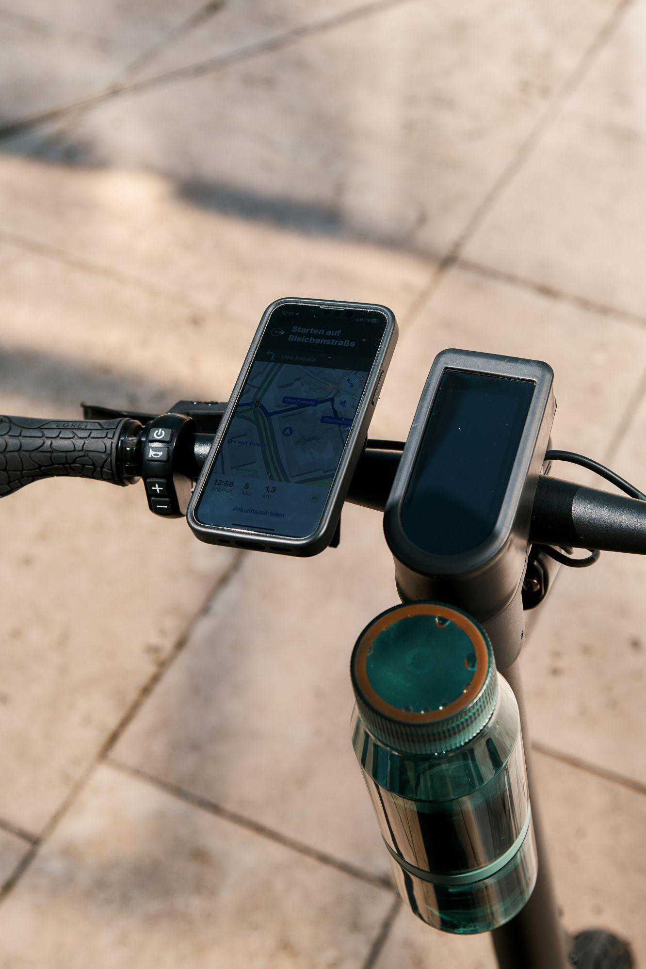 Lenker eines Elektrorollers mit Smartphone-Navigation und Wasserflasche.