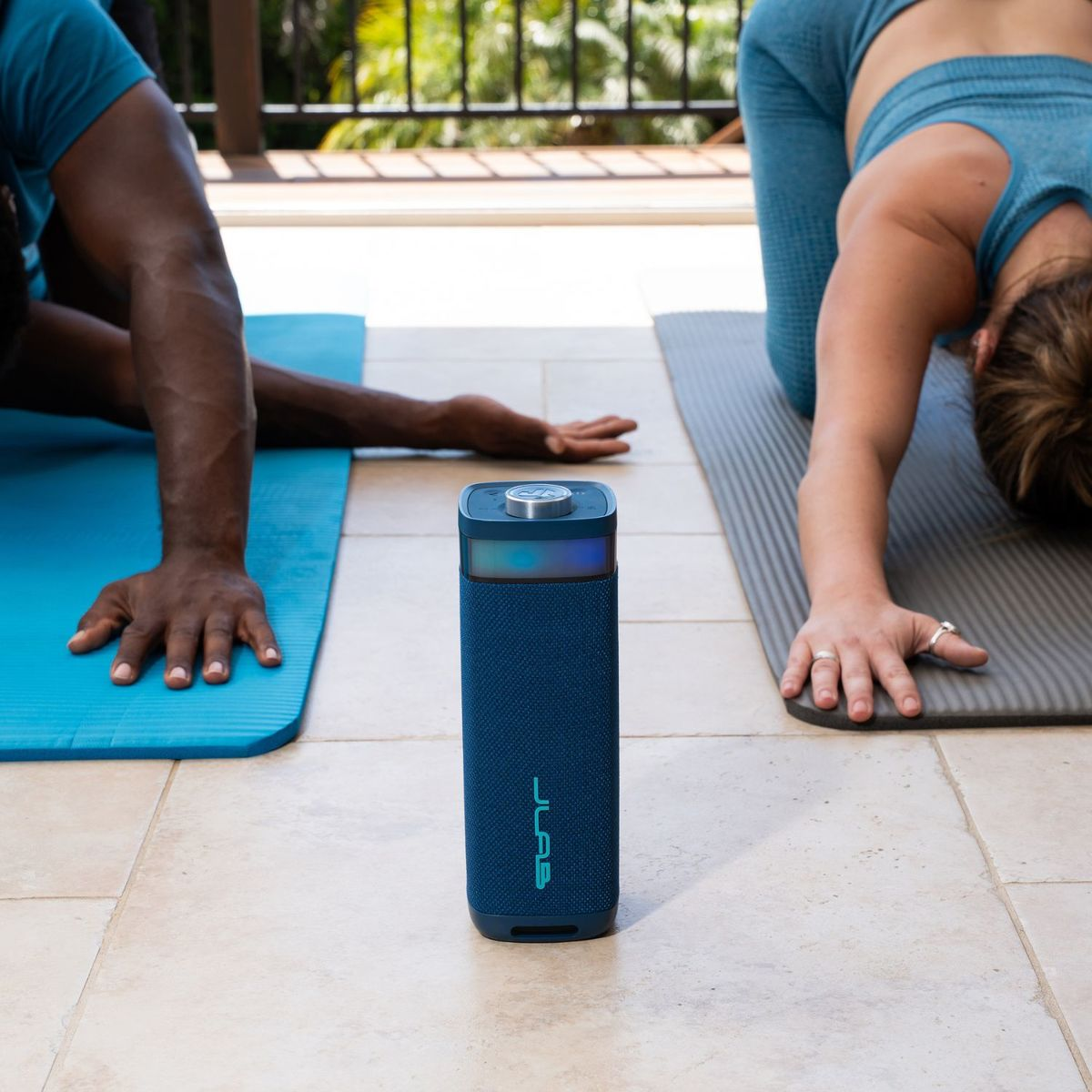 Zwei Personen machen Yoga auf Matten, ein blauer Lautsprecher steht dazwischen.