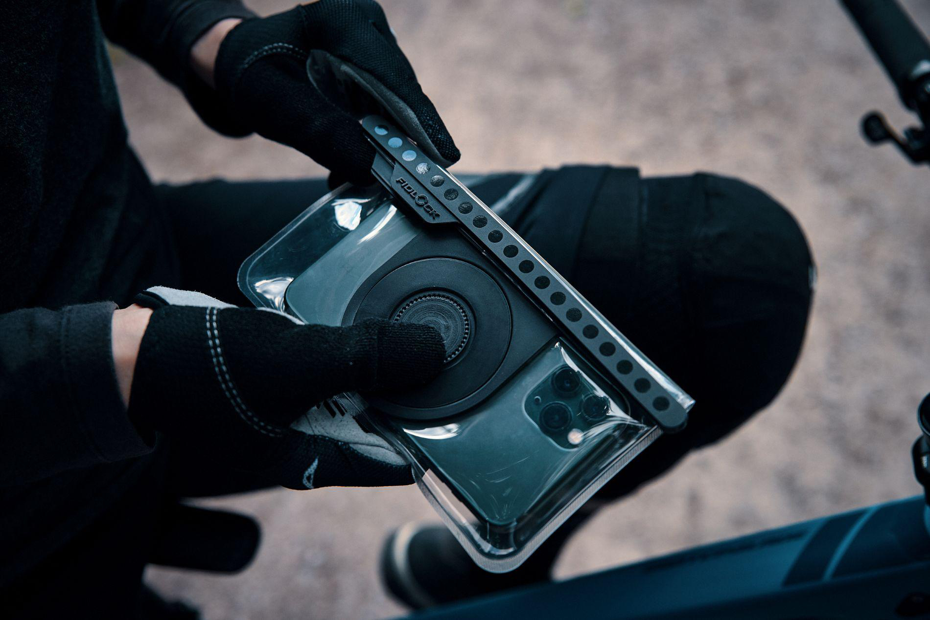 Person in schwarzen Handschuhen hält ein Handy in einer Hülle mit schwarzer Halterung.