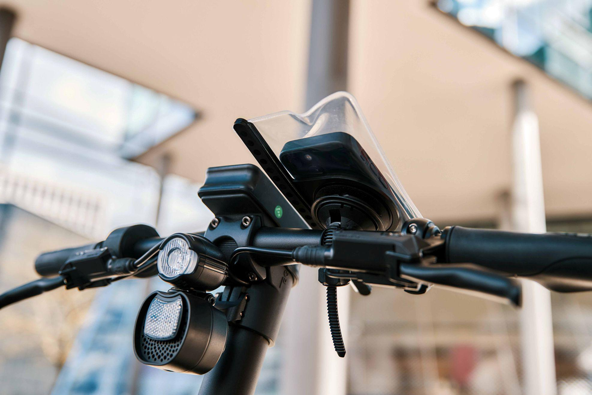 Nahaufnahme des Lenkers eines Elektrorollers mit Lichtern und Handyhalterung.