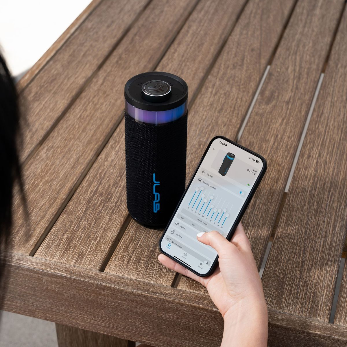 Ein schwarzer Lautsprecher mit blauer Beleuchtung neben einem Smartphone, das eine App anzeigt.