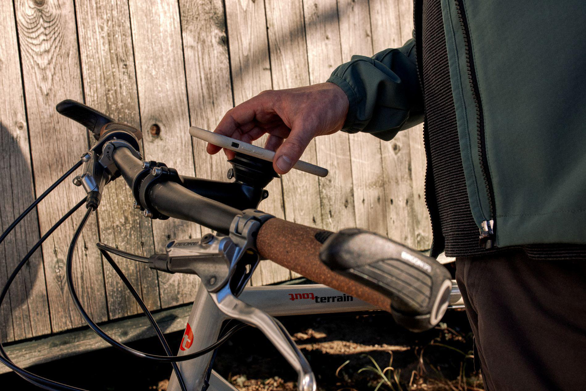 Mann hält Smartphone auf Fahrradlenker vor Holzwand.