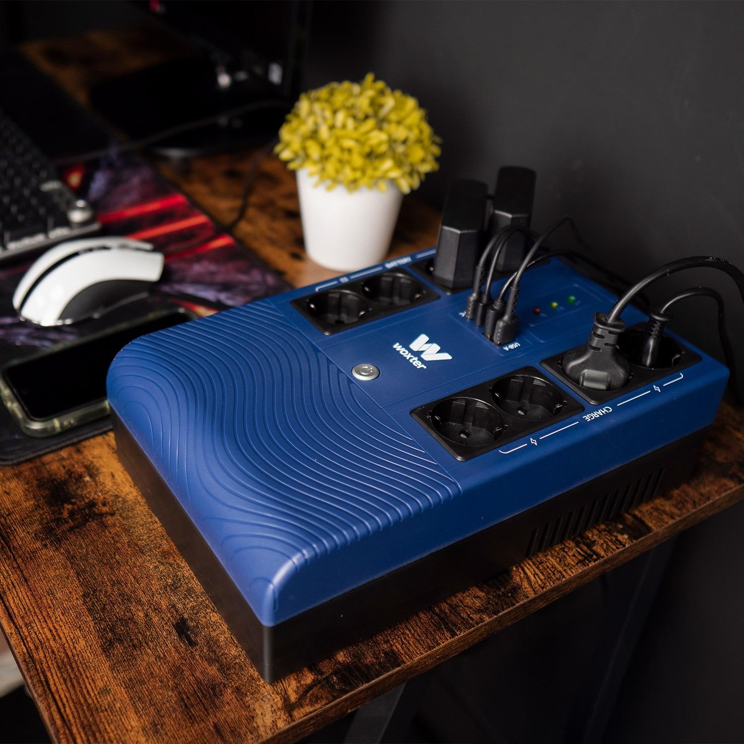 Regleta azul con cables y enchufes sobre un escritorio de madera junto a un ordenador.