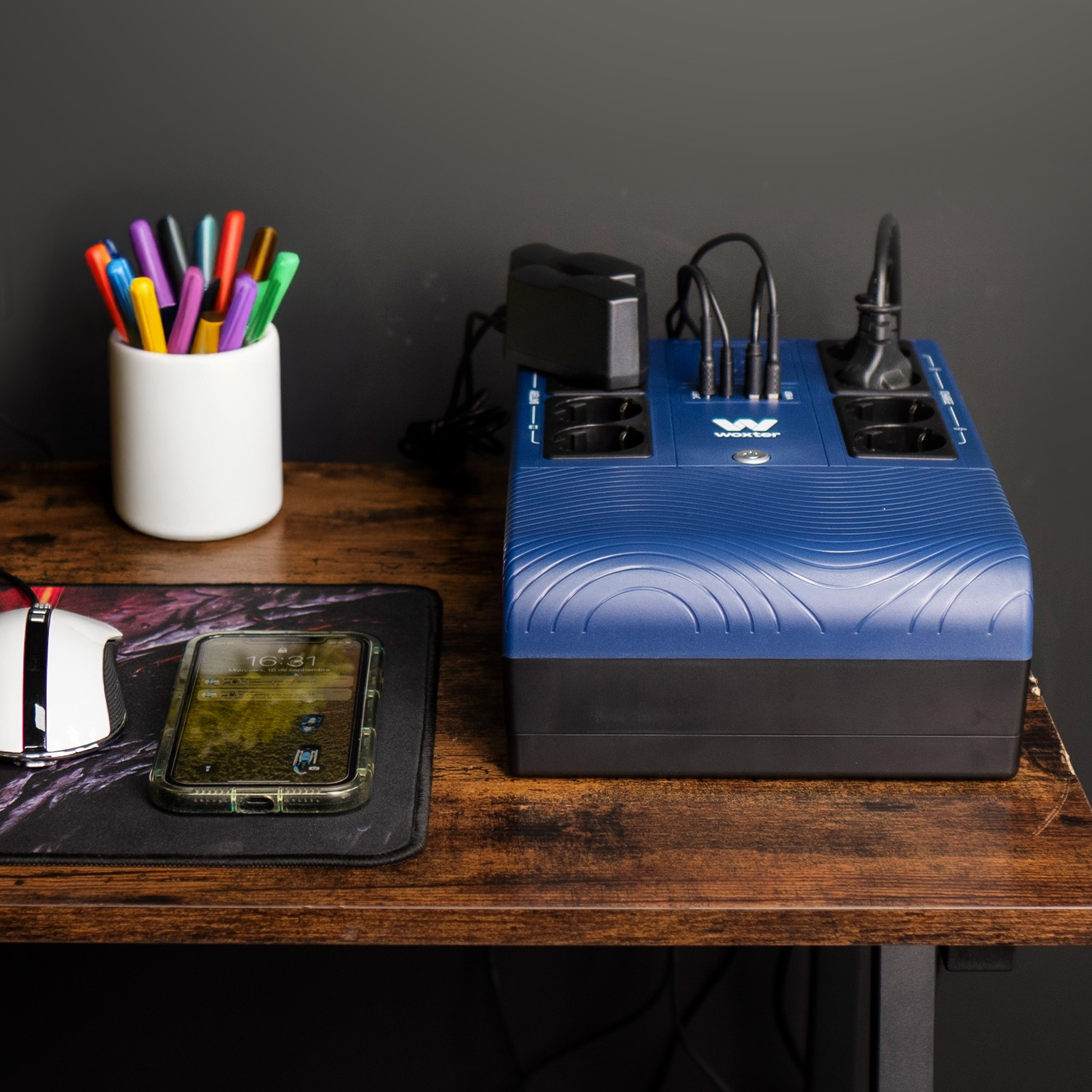 Una regleta azul con puertos USB está sobre un escritorio de madera junto a un teléfono y bolígrafos.