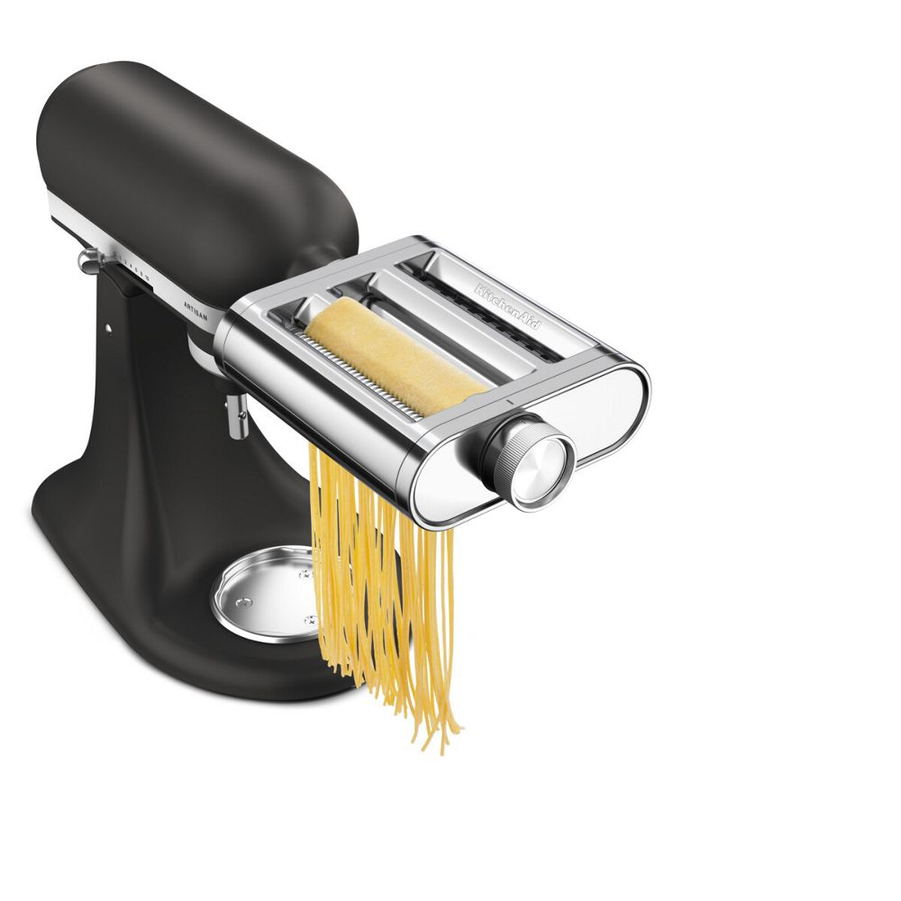 Batidora KitchenAid negra con accesorio para pasta plateado creando espaguetis frescos.